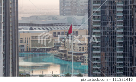 Aerial view of Dubai Fountain in downtown with palms in park next to shopping mall and souq night to day timelapse, UAE 111581416