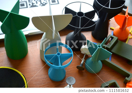 Prototype model of rocket bomb tip printed on 3D printer. Small colored models of tail fins, tail cone printed on 3D printer from molten plastic on table. New modern innovation printing technology 111581632