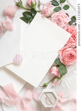 Blank card and envelope near pink roses and silk ribbons top view, wedding mockup 111581973
