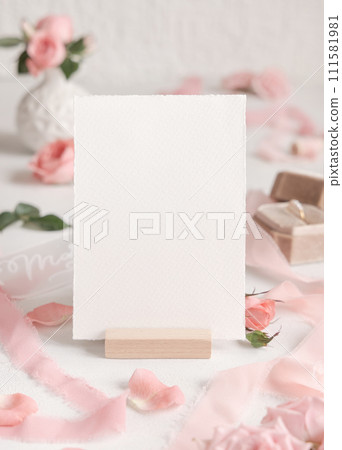Blank card near light pink roses, petals and silk ribbons close up, wedding mockup 111581981
