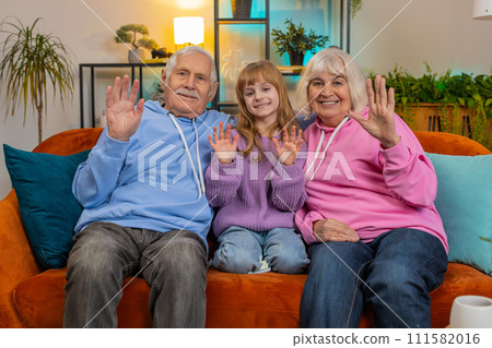 Child girl granddaughter with grandparents bloggers waves hand hello hi relaxing making on home sofa 111582016