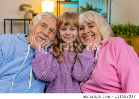 Portrait of smiling kid granddaughter and loving grandfather and grandmother looking at camera home Portrait of smiling kid granddaughter and loving grandfather and grandmother looking at camera home 111582017