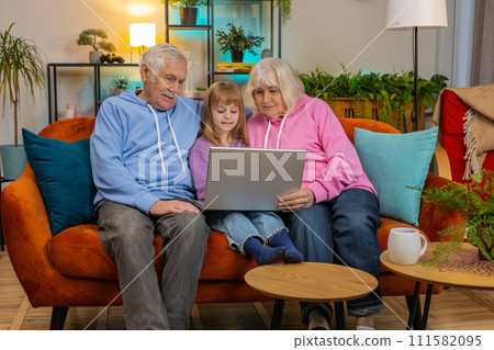 Senior couple man and woman with child girl granddaughter spending time at home sofa using laptop 111582095
