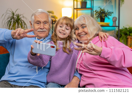 Child girl granddaughter with grandparents make blogger selfie smartphone portrait shows peace sign 111582121