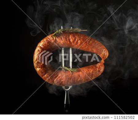 Hot smoked meat sausage on a fork with rosemary. Concept of cooking and serving smoked sausage in inn or tavern Hot smoked meat sausage on a fork with rosemary. Concept of cooking and serving smoked sausage in inn or tavern 111582502