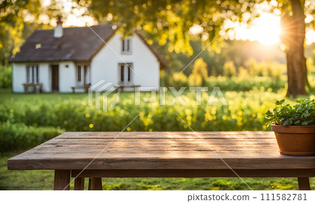 An empty wooden table in the foreground, with a blurred country house in the background against a verdant garden setting An empty wooden table in the foreground, with a blurred country house in the background against a verdant garden setting 111582781