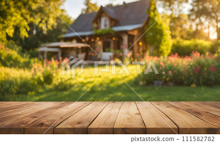 An empty wooden table in the foreground, with a blurred country house in the background against a verdant garden setting An empty wooden table in the foreground, with a blurred country house in the background against a verdant garden setting 111582782