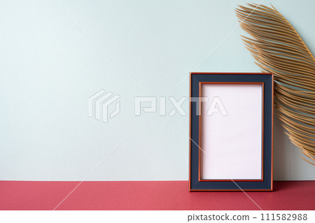 Navy photo frame with green leaf on red shelf. gray wall background 111582988