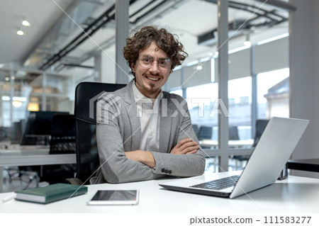 A professional young businessman with curly hair confidently working at his laptop in a contemporary office environment. A professional young businessman with curly hair confidently working at his laptop in a contemporary office environment. 111583277