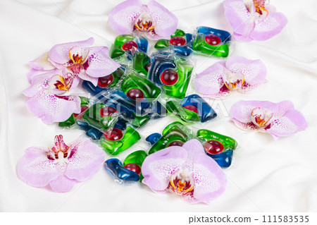 Laundry capsules among orchid flowers on satin fabric. 111583535