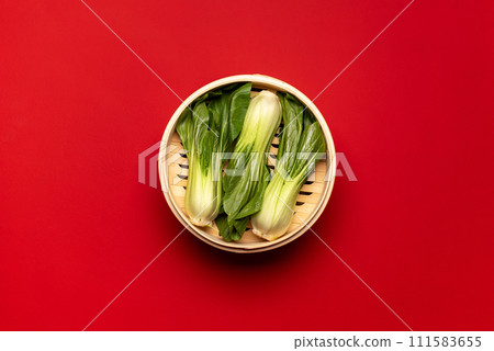 Bok choy cooked in bamboo steamer, above view on a red table Bok choy cooked in bamboo steamer, above view on a red table 111583655