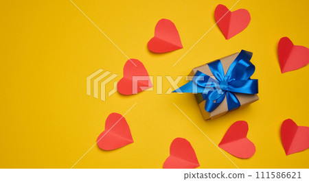 Gift box with red satin ribbon and bow on a yellow background. Holiday background Gift box with red satin ribbon and bow on a yellow background. Holiday background 111586621