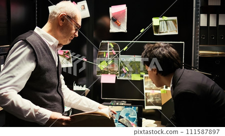 Police officers on duty at agency, reviewing surveillance footage for suspect identification in incident room. Two partners trying to find culprit with incriminating proof, gather intelligence. 111587897