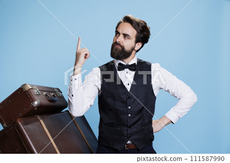 Male bellhop worker getting an idea, finding solution in front of camera next to trolley bags. Hotel porter in formal clothes being genius and thinking about something to solve problems. 111587990