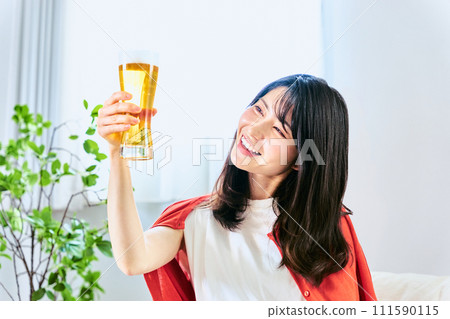 一名 30 多歲的女士盯著一瓶啤酒，手裡拿著它，試圖在家中獨自喝酒，以在假期明媚的午後時光中恢復活力。 111590115