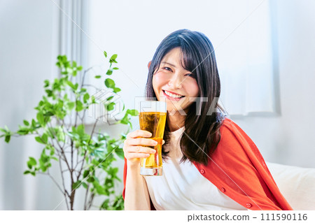 一位 20 多歲到 30 多歲的微笑女性在假期的明亮時間裡看著鏡頭，獨自在家裡的房間裡喝啤酒 111590116