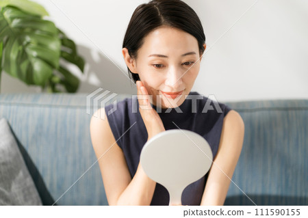 A woman in her 30s sitting on a sofa and looking in a mirror 111590155