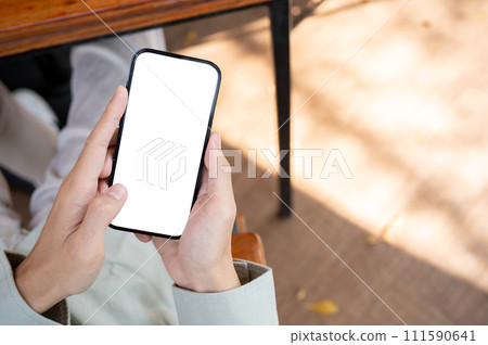 A man using his smartphone at a table in a cafe, with a white-screen smartphone mockup. A man using his smartphone at a table in a cafe, with a white-screen smartphone mockup. 111590641