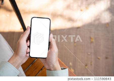 A man using his smartphone at a table in a cafe, with a white-screen smartphone mockup. A man using his smartphone at a table in a cafe, with a white-screen smartphone mockup. 111590643