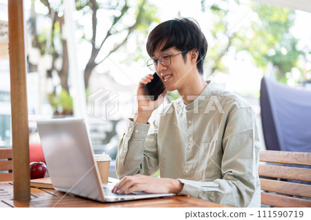 A man is discussing business on the phone with his client while working remotely at a coffee shop A man is discussing business on the phone with his client while working remotely at a coffee shop 111590719