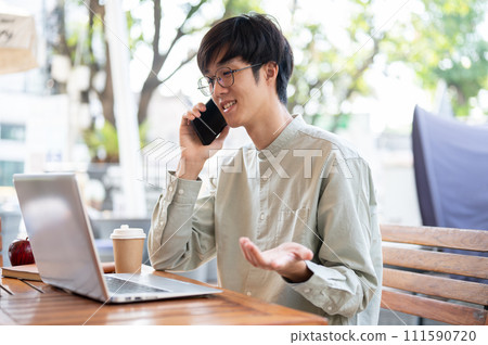 A man is discussing business on the phone with his client while working remotely at a coffee shop 111590720