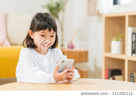 An elementary school girl operating a smartphone. 111592112