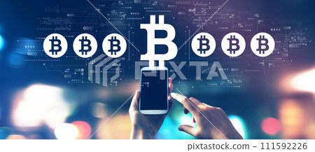 Bitcoin theme with a smartphone in city lights at night Bitcoin theme with a smartphone in city lights at night 111592226