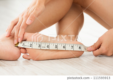 A woman measuring the soles of her feet with a tape measure 111593913