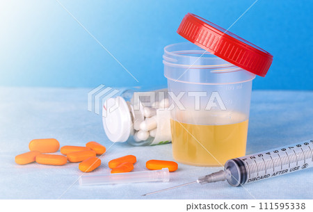 Urine container, syringe and colored pills on blue background on sunlight 111595338