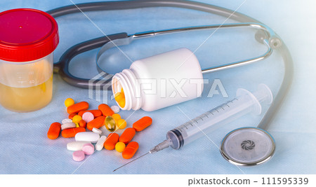 Urine container, syringe, phonedoscope and colored pills on blue background. 111595339