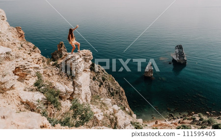 Woman travel sea. Happy tourist enjoy taking picture outdoors for memories. Woman traveler looks at the edge of the cliff on the sea bay of mountains, sharing travel adventure journey 111595405