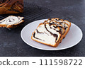Pieces of fresh homemade braided bun with poppy seeds on white plate, black background, close up 111598722