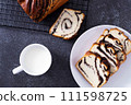 Pieces of bun with poppy seeds on white plate with mug of milk at black background, top view 111598725