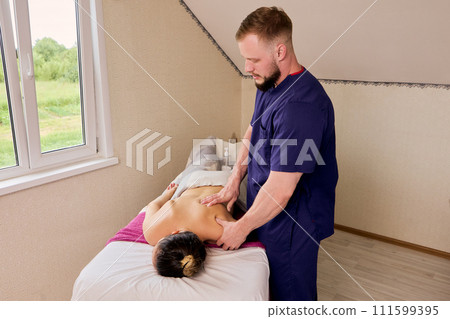 Massage therapist giving massage to white woman talking about belly on massage table. 111599395