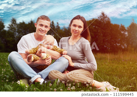 Twenty year old married couple with baby is sitting on grass of country lawn. Twenty year old married couple with baby is sitting on grass of country lawn. 111599445