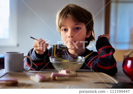 Unhappy male child sits in kitchen table with bowl of cereal in dimly lit kitchen. Unhappy male child sits in kitchen table with bowl of cereal in dimly lit kitchen. 111599447