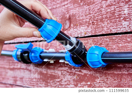 An external water supply system connected by compression fittings is mounted on weathered wall of red wooden house. An external water supply system connected by compression fittings is mounted on weathered wall of red wooden house. 111599635