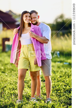 Vertical family portrait, young couple poses while standing in courtyard of country house on summer evening. 111599649