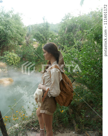 A woman standing next to a river with a backpack on her back A woman standing next to a river with a backpack on her back 111601172