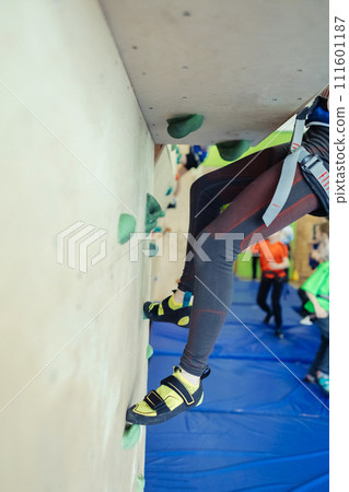 Rock climbing for children. Blond boy in a green shirt is climbing climbing wall. Bouldering class. Artificial track for safe activities and competitions. Mountaineering, safety system, special shoes Rock climbing for children. Blond boy in a green shirt is climbing climbing wall. Bouldering class. Artificial track for safe activities and competitions. Mountaineering, safety system, special shoes 111601187