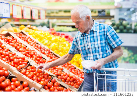 Mature senor considering tomatoes in vegetables section of supermarket Mature senor considering tomatoes in vegetables section of supermarket 111601222