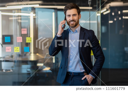 Mature businessman in a suit engaged in a phone conversation while working in a contemporary office setting. 111601779