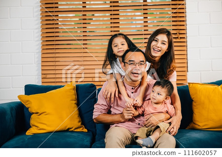 In their modern home a smiling family enjoys quality time on the sofa showcasing togetherness. Parents daughters and siblings bond laugh and embrace in a heartwarming family portrait. In their modern home a smiling family enjoys quality time on the sofa showcasing togetherness. Parents daughters and siblings bond laugh and embrace in a heartwarming family portrait. 111602057