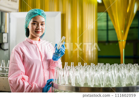 A uniformed QC woman specializing in chemical science ensures top-tier quality for juice drinks by meticulously examining glass bottles in the beverage factory industry. A uniformed QC woman specializing in chemical science ensures top-tier quality for juice drinks by meticulously examining glass bottles in the beverage factory industry. 111602059