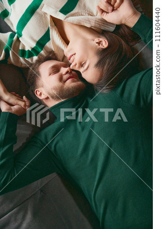 View from above. Photo of young, cute couple lying down on sofa facing each other, close and smiling, sharing tender moment. View from above. Photo of young, cute couple lying down on sofa facing each other, close and smiling, sharing tender moment. 111604440