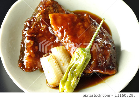 Overhead shot of yellowtail teriyaki and fried shishito and green onions against a black background 111605293