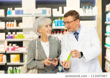 Middle-aged male pharmacist consulting old woman costumer about care product in box 111605967
