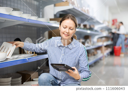 Woman in supermarket is choosing square plates 111606043