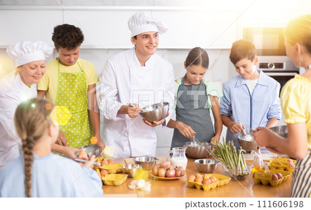 Young guy and adult woman cook teaches group of children to cook Young guy and adult woman cook teaches group of children to cook 111606198