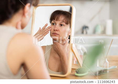 Woman inspecting facial skin in mirror during daily routine Woman inspecting facial skin in mirror during daily routine 111606243